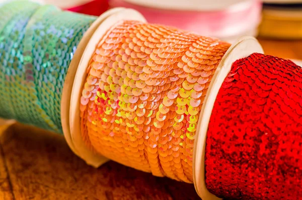 Gros plan de rouleaux brillants de ruban paillettes coloré, multicolore sur une table en bois dans un fond flou — Photo