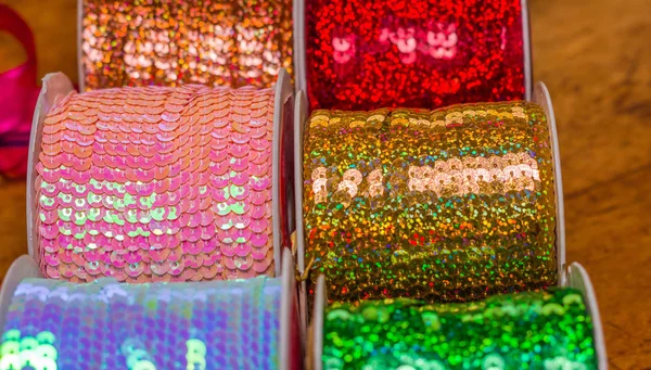 Primer plano de rollos brillantes de cinta de lentejuelas de colores, multicolor sobre una mesa de madera en un fondo borroso —  Fotos de Stock