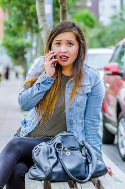 Jean ceket ve siyah tayt giyen, cep telefonunu kullanarak ve şok duygu gösteren moda trendy rahat genç kadın. Şok yüz ifadesi ile kadın portre
