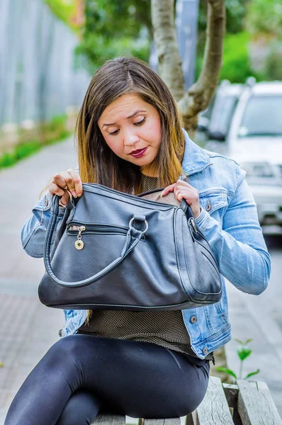 Bir şey arka plan bulanık çantasında içinde ararken bir jean ceket ve siyah tozluk, genel bir sandalyede oturuyor giyen moda trendy rahat genç kadın — Stok fotoğraf