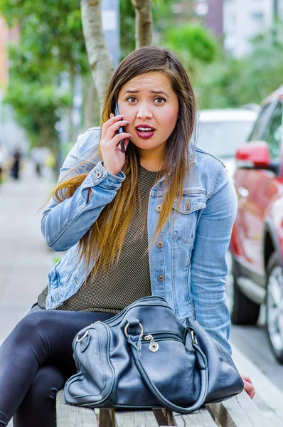 Mode trendy lässig junge Frau trägt eine Jeansjacke und schwarze Leggings, nutzt ihr Handy und zeigt Schock Emotionen. Frauenporträt mit schockiertem Gesichtsausdruck — Stockfoto