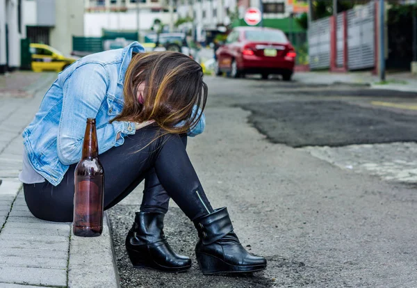 Bela jovem bêbada sentada em uma calçada com garrafa de cerveja na mão dormindo ao ar livre, mulher desesperada e conceito de viciada — Fotografia de Stock