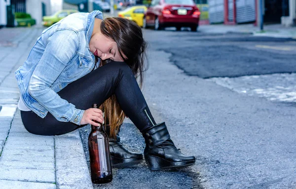 Hermosa joven borracha sentada en una acera con una botella de cerveza en la mano durmiendo al aire libre, mujer desesperada y concepto adicto —  Fotos de Stock