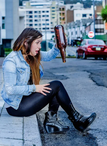 Mooie jonge dronken vrouw zitten in een trottoir met fles bier in haar hand, desesperate vrouw en verslaafde concept — Stockfoto