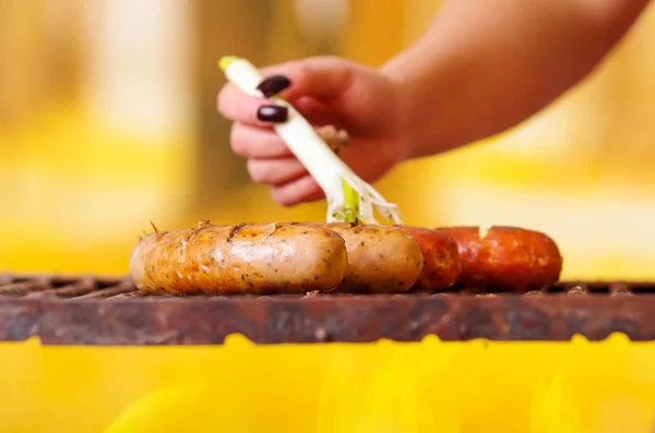 Close up of woman s hand holding a long white onion adding oil to a grilling sausages on barbecue grill. BBQ in the garden. Bavarian sausages — Stock Photo, Image