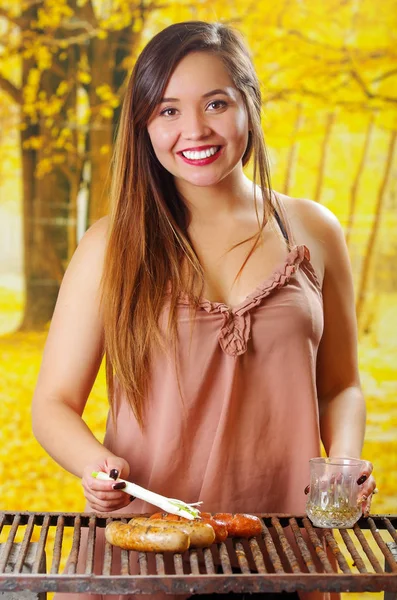 Крупный план красивой молодой улыбчивой женщины, использующей длинный белый лук на гриле колбасы на гриле барбекю. Барбекю в саду. Баварские сосиски на размытом фоне — стоковое фото