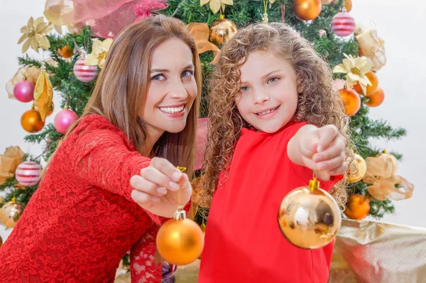 Close up of happy girl decorating Christmas tree with her mom pointing in front of them golden christmas balls, family christmas concept — Stock Photo, Image