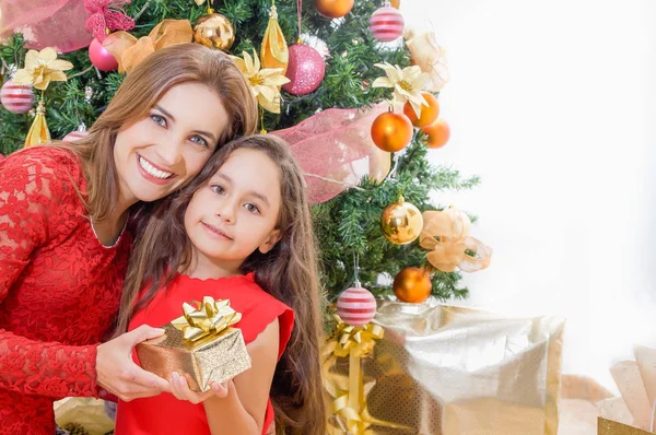 Primer plano de mamá e hija felices sosteniendo un regalo frente a un árbol de Navidad, concepto de Navidad — Foto de Stock