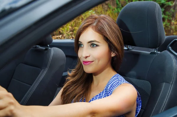 Крупним планом красива молода жінка всередині чорного автомобіля, керуючи машиною однією рукою, на розмитому фоні природи — стокове фото
