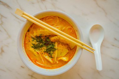 Penang asam laksa pirinç noodle yemek çubukları ile beyaz kase görünümünü baharatlı balık demirhindi çorba beyaz porselen kaşık ve Singapur taze otlar ile beyaz tabloda yukarıda
