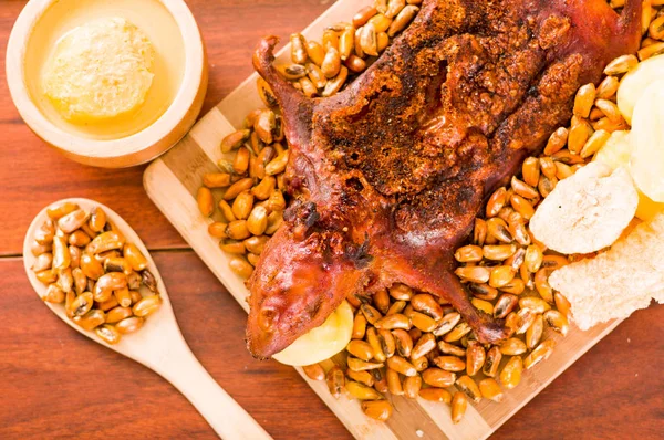 Primer plano plato tradicional ecuatoriano, conejillo de indias a la parrilla extendido sobre tabla de madera, tostados y salsa al lado, visto desde arriba — Foto de Stock