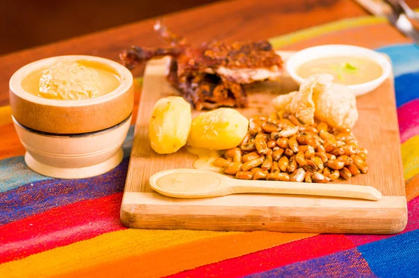 Cut pieces cooked guine pig meat lying on wooden surface next to potatoes, tostados and bowl of salsa — Stock Photo, Image