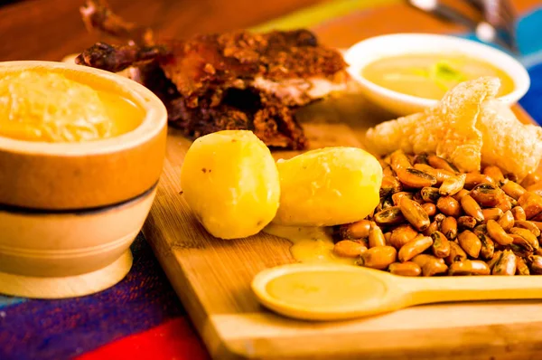 Cut pieces cooked guine pig meat lying on wooden surface next to potatoes, tostados and bowl of salsa — Stock Photo, Image