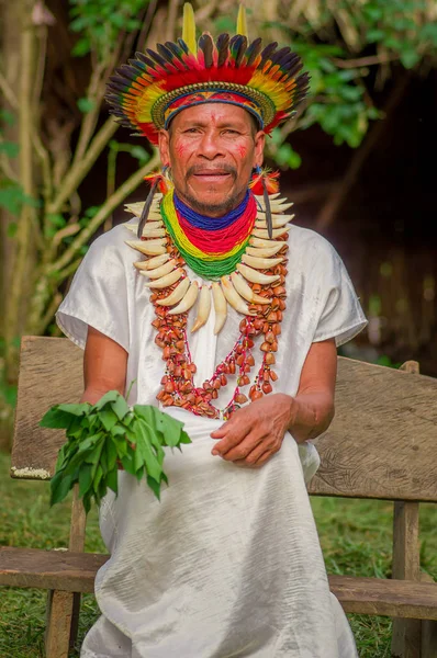 LAGO AGRIO, ECUADOR - NOVEMBER 17, 2016: Siona shaman sitting in a chair with a traditional dress with a feather hat in an indigenous village in the Cuyabeno Wildlife Reserve — Stock Photo, Image