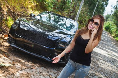 Sorunlu bir ROADTRIP Siyah araba cep telefonunu kullanarak ve sunglases, siyah t-shirt ve jeans, giyen güzel beyaz kadının kapatın. Kadın üzerinde ısınmış duygusal tepki