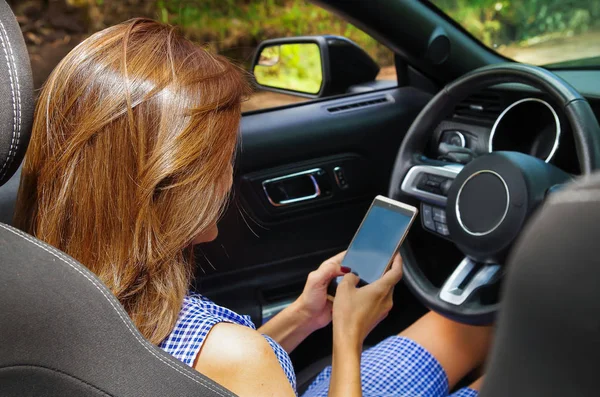 Närbild av vackra kaukasiska kvinna med hennes mobiltelefon inuti den svarta bilen i en suddig natur bakgrund — Stockfoto