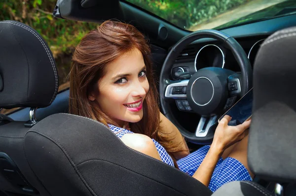 Närbild av vackra kaukasiska kvinna med hennes mobiltelefon inuti den svarta bilen och tittar på kameran i en suddig bakgrund — Stockfoto