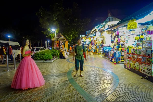 AO NANG, TAILANDIA - 09 DE FEBRERO DE 2018: Vista al aire libre de un hombre no identificado caminando en una acera cerca de una mujer con un vestido rosa en la calle Ao Nang durante la noche en AO Nang — Foto de Stock