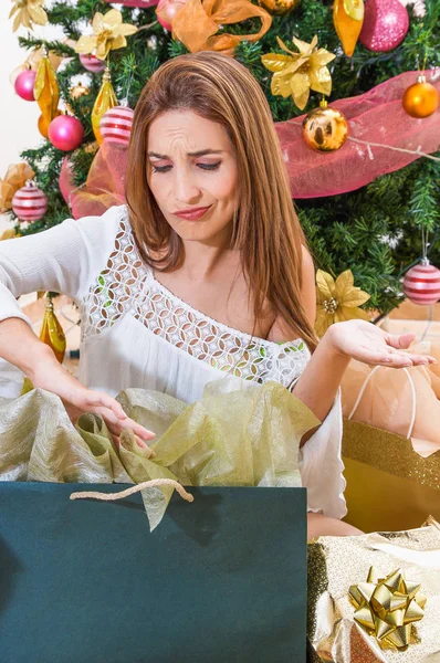 Primo piano di una donna stressante che fa facce divertenti, indossa una camicetta bianca davanti a un albero di Natale, alloggia i regali, albero di Natale e felice anno nuovo concetto — Foto Stock