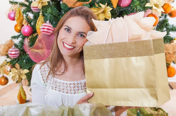 Крупним планом красива усміхнена жінка в білій блузці перед ялинкою, і тримає в руках подарунок, весела різдвяна та щаслива концепція нового року — стокове фото