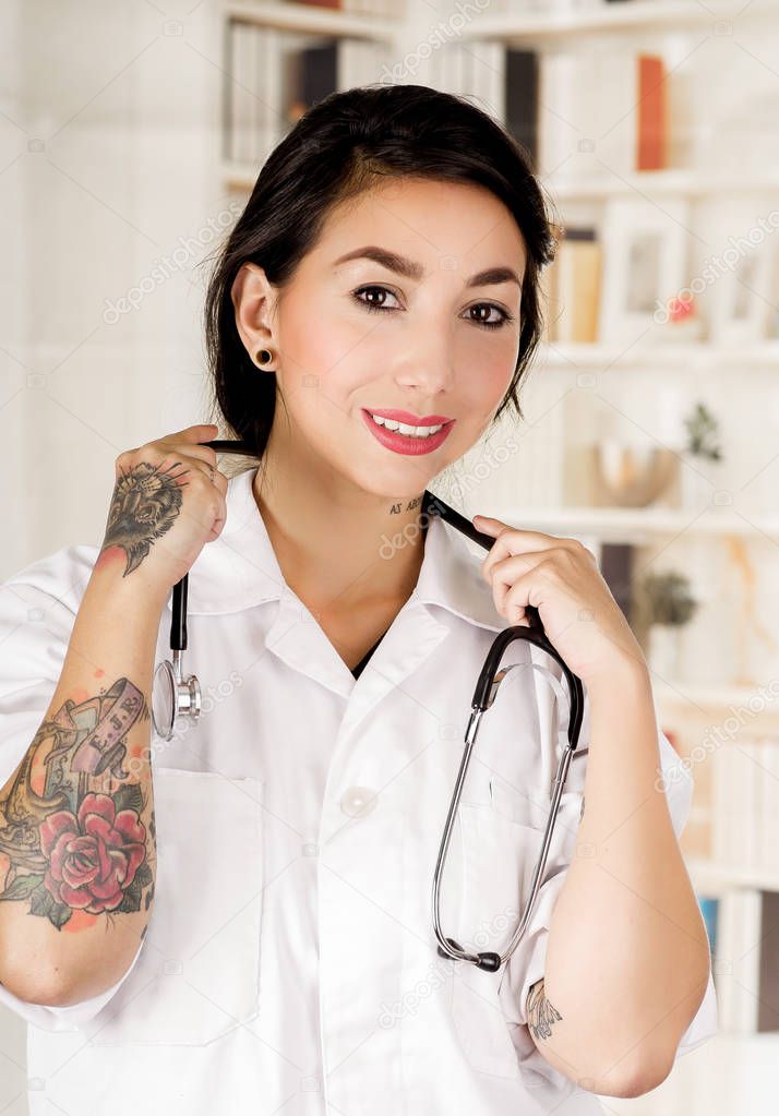 Beautiful tattooed young doctor with a stethoscope around her neck, in office background