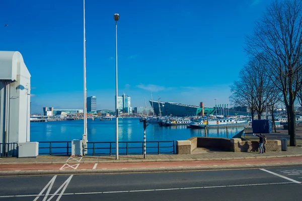 AMSTERDAM, PAYS-BAS, 10 MARS 2018 : Bâtiments anciens et bateaux traditionnels au bord de la rivière et vue extérieure sur les rues d'Amsterdam — Photo