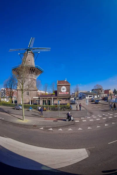 AMSTERDAM, PAÍSES BAJOS, 10 DE MARZO DE 2018: Magnífica vista al aire libre de personas no identificadas caminando cerca del molino de viento De Gooyer, el molino de madera más alto de los Países Bajos Amsterdam — Foto de Stock