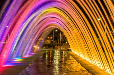 QUITO, ECUADOR- FEBRUARY 22, 2018: Beautiful outdoor view of colorful water entertainment structure fountain in form of arch with buildings behind clipart