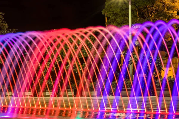 QUITO, ECUADOR - 22 DE FEBRERO DE 2018: Hermosa vista al aire libre de la colorida fuente de la estructura de entretenimiento acuático, a larga exposición en la noche, con edificios detrás —  Fotos de Stock