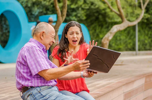 Vista al aire libre de la celebración del padre y la computadora y sacry hija gritando miedo de su padre tirar la computadora en el suelo, en el parque —  Fotos de Stock