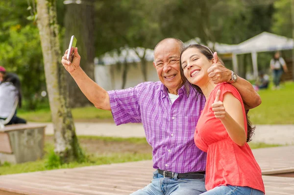 Vista al aire libre de padre e hija usando un teléfono celular, tomando una selfie en el parque —  Fotos de Stock