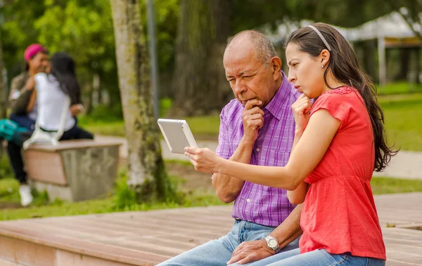 Vista al aire libre de padre e hija usando una tableta buscando algo interesante, en el parque —  Fotos de Stock
