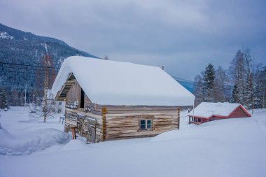 View of traditional wooden houses covered with snow in stunning nature background and huge mountain behind in Norway clipart