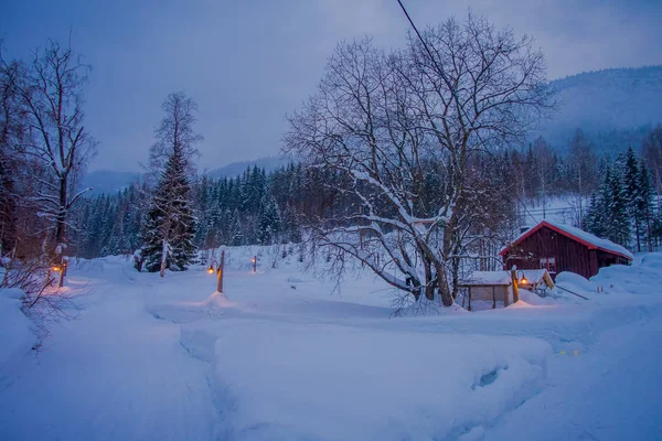 Niesamowity widok nocny tradycyjnych drewnianych domów ze śniegiem w dachu w przepięknym tle przyrody, z kilkoma światłami i słupkami na zewnątrz w regionie Valdres w Norwegii — Zdjęcie stockowe