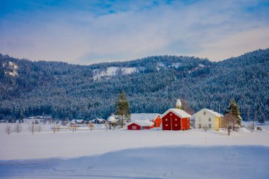 Astonishing outdoor view of traditional Norwegian mountain red houses of wood covered with snow in the roof in stunning nature mountain background in Norway clipart