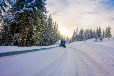 Reinli, Norveç - 26 Mart 2018: Kar temizleme makinesinin açık hava manzarası, sabah karlarla kaplı ağaçlar ve yollarda kardan yolun sokaklarını temizler, ufukta gün doğumu
