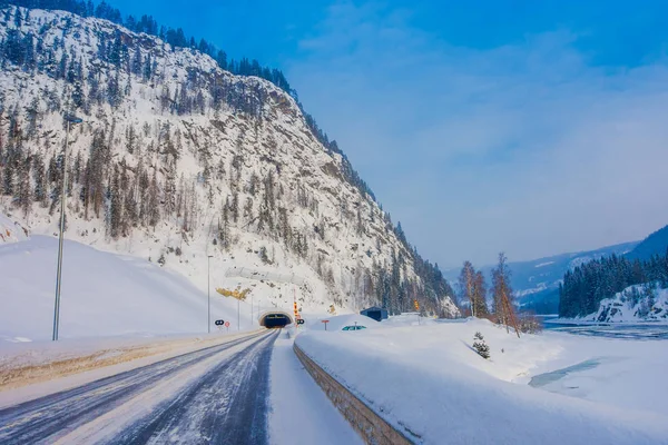 Reinli, Norway - March 26, 2018: Outdoor view of winter road snow and ice in the forest, with informative sign at the enter of a tunnel in Norway — Stock Photo, Image