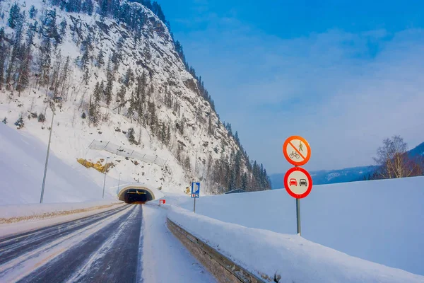 Reinli, Norvegia - 26 marzo 2018: Veduta esterna della strada invernale neve e ghiaccio nella foresta, con cartello informativo all'ingresso di una galleria in Norvegia — Foto Stock