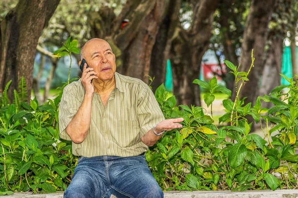 Вид на улицу старика сидит на скамейке, пользуясь мобильным телефоном и наслаждаясь природой. Все проблемы остались позади — стоковое фото