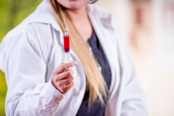 Nahaufnahme einer Frau, die einen Labormantel trägt und eine Spritze mit Blut in der Hand hält — Stockfoto