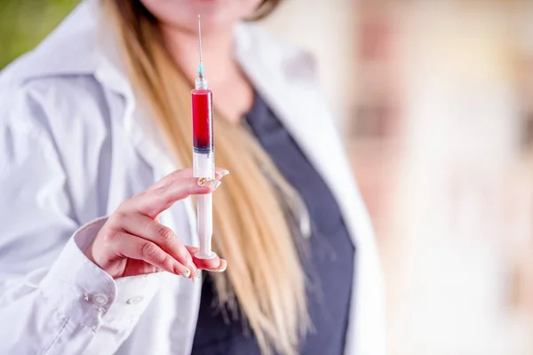 Close up van vrouw draagt een laboratoriumjas en houdt van een spuit met bloed in haar hand — Stockfoto