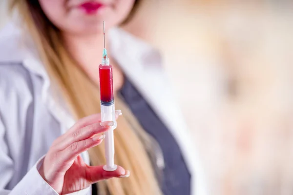 Nahaufnahme einer verschwommenen lächelnden schönen jungen Frau, die einen Labormantel trägt und eine Spritze mit Blut in der Hand hält — Stockfoto