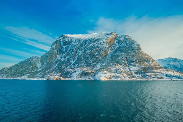 Vista esterna di scene costiere di enormi montagne parzialmente coperte di neve durig un viaggio a Hurtigruten in un cielo blu — Foto Stock