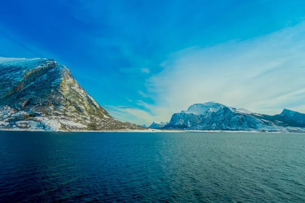 Vista esterna di scene costiere di enormi montagne parzialmente coperte di neve durig un viaggio a Hurtigruten in un cielo blu — Foto Stock