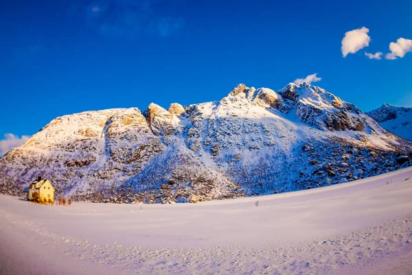 雪に覆われた冬の北極圏で雪との背後にある巨大な山で覆われた白い木造の家の屋外の表示 — ストック写真