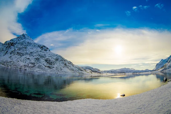 Linda vista ao ar livre de água limpa em um lago com um sol refletindo, com uma enorme montanha coberta de neve nas Ilhas Lofoten — Fotografia de Stock