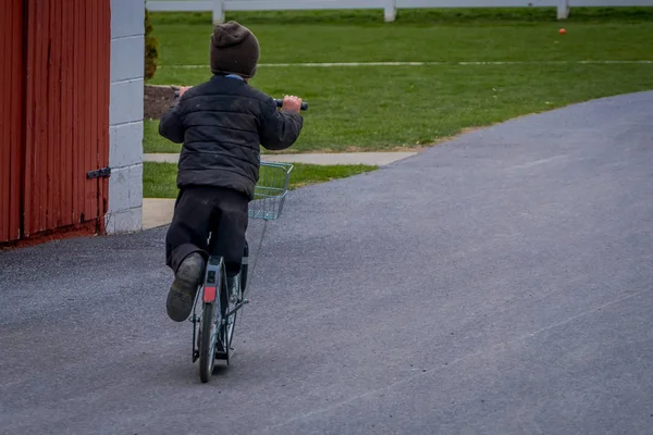 Невідомий маленький амішів хлопчик грає зі своїми роликами або скутерами на задньому дворі свого будинку — стокове фото