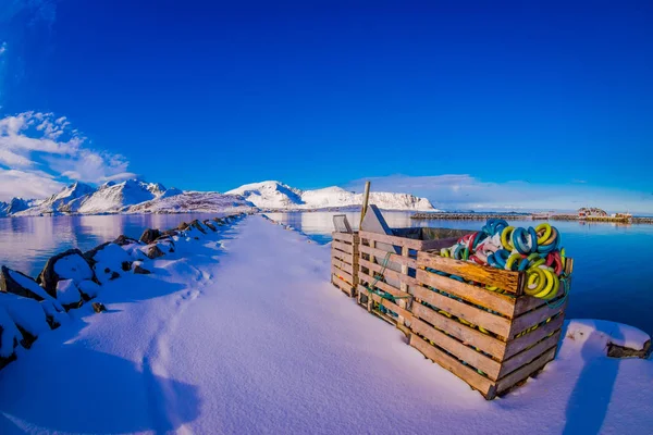 Outdoor scenic view with rocks covered with snow close to a lake and colorful plastic floating material used for net inside of wooden box in Svolvaer — Stock Photo, Image