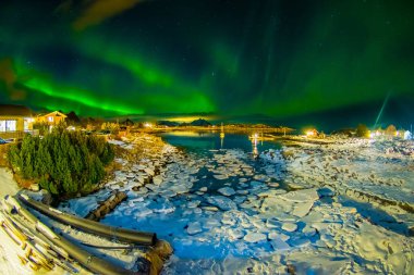 Amazing outdoor view of green aurora borealis in the sky during night and small and medium pieces of Ice left behind during a low tide on a frozen lake clipart