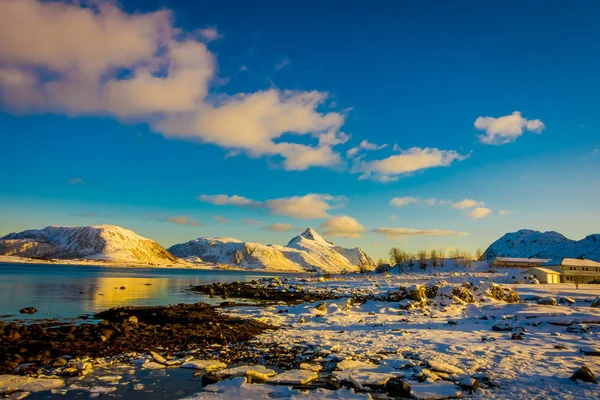Pôr do sol na costa de Henningsvaer com enormes montanhas cobertas de neve em um lindo céu azul nas Ilhas Lofoten, Austvagoya — Fotografia de Stock